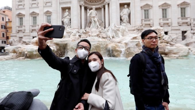 Tourists wearing protective masks take a selfie in front of ther Trevi's Fountain after two cases of coronavirus were confirmed in Italy