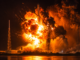 Explosión de un cohete durante una prueba o lanzamiento nocturno en una plataforma espacial, generando una enorme bola de fuego y columnas de humo.