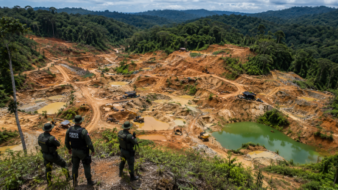 Vista aérea de Crucitas con extensas áreas afectadas por minería ilegal mientras oficiales observan la zona desde un punto elevado.