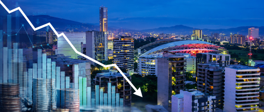 Vista panorámica de San José con gráficos financieros descendentes que representan la desaceleración económica y la contracción del mercado laboral en Costa Rica.