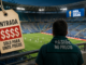 Aficionado observa un partido del Mundial 2026 mientras una etiqueta simboliza el alto costo de las entradas.