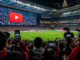 Aficionados y creadores de contenido siguen un partido en un estadio mientras YouTube se consolida como plataforma clave para el Mundial 2026.