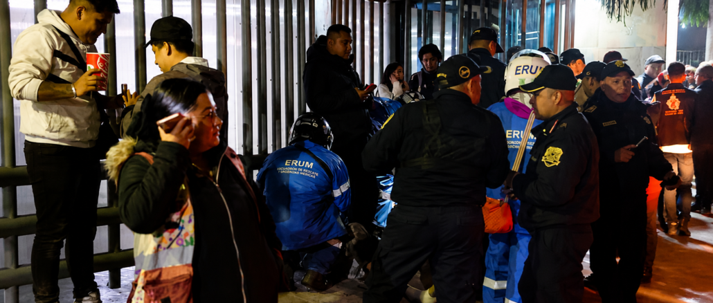 Policías y paramédicos atienden una emergencia mientras varias personas observan en las afueras de un edificio durante un operativo nocturno.