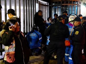 Policías y paramédicos atienden una emergencia mientras varias personas observan en las afueras de un edificio durante un operativo nocturno.