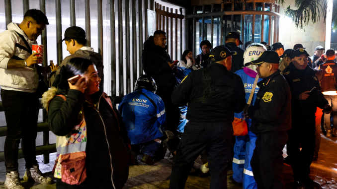 Policías y paramédicos atienden una emergencia mientras varias personas observan en las afueras de un edificio durante un operativo nocturno.