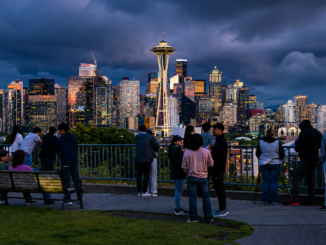 Vista panorámica del centro de Seattle al atardecer con la Space Needle y personas observando el horizonte desde un mirador urbano.