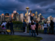 Vista panorámica del centro de Seattle al atardecer con la Space Needle y personas observando el horizonte desde un mirador urbano.