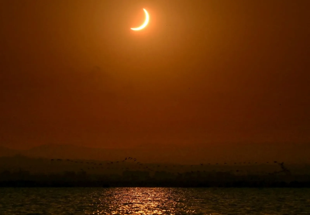 La Luna descubre el Sol tras la fase de totalidad del eclipse solar, mientras una bandada de pájaros…