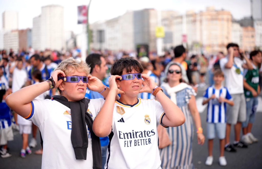 Aficionados del Real Madrid observan el eclipse solar con gafas especiales antes del partido del Trofeo Teresa Herrera en el Estadio Riazor.